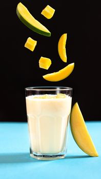 Lassi is a popular traditional dahi, yogurt based cold drink in India. Lassi consists of yogurt, water, spices and sometimes fruit and ice. Fruit levitation. Mango slices on black background