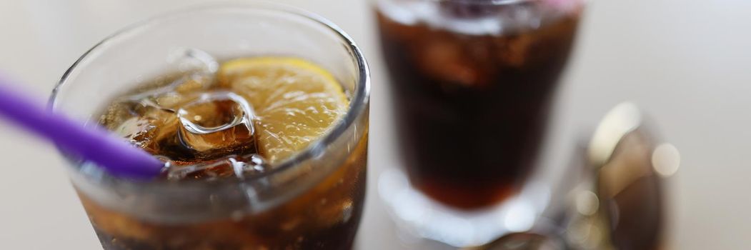 Close-up of pair of glasses filled with coca cola with lemon and ice cubes, cooling summertime drinks. Refreshing beverages in hot weather. Thirsty concept