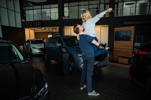 Happy caucasian couple hugging while buying a new car in a car dealership