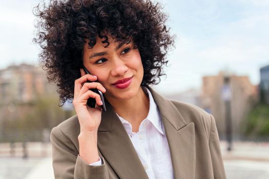 smiling latin woman talking by mobile phone, concept of communication and urban lifestyle, copy space for text