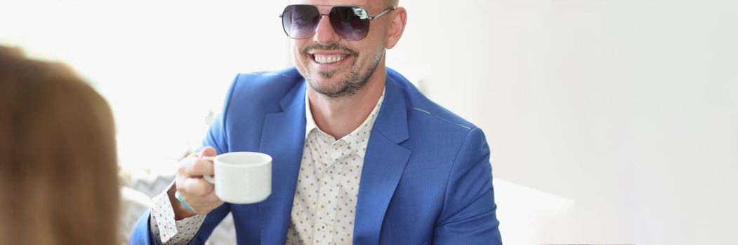 Portrait of well dressed smiling man drinking coffee in cafe on business meeting with partner. Cheerful middle aged guy in posh suit. Lunch, deal concept