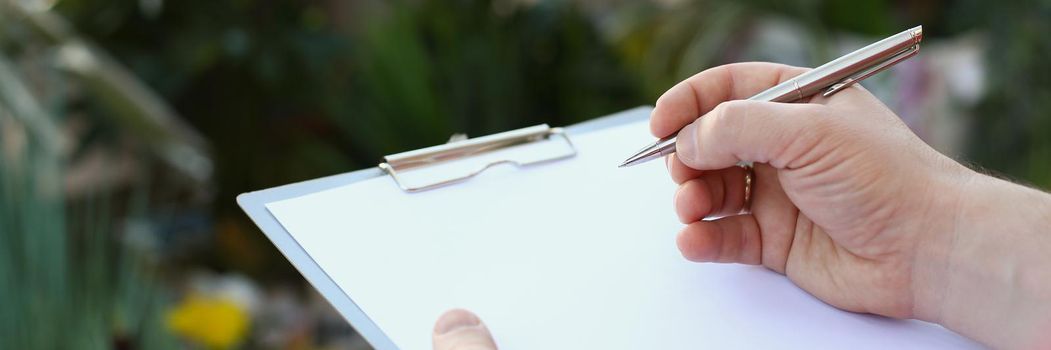Close-up of human hand writing on clipboard with white paper, pen and blank document. Business paperwork or making notes, sign document. Business concept
