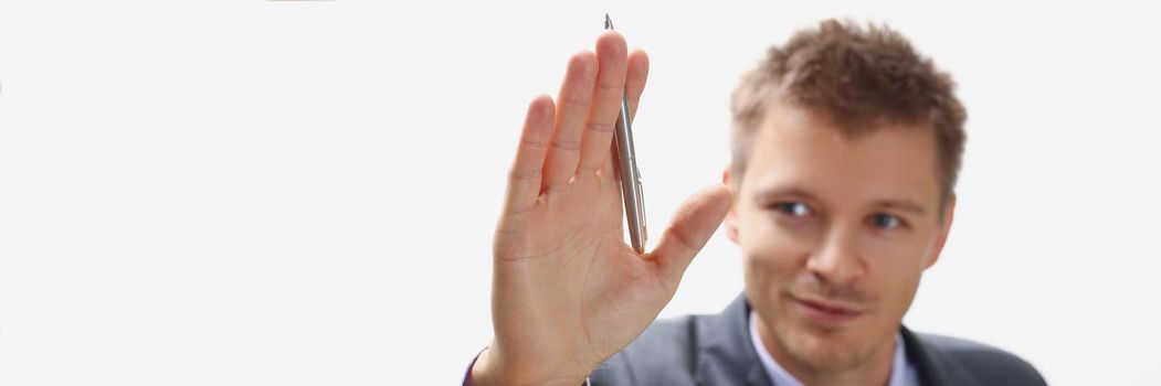 Portrait of handsome businessman wave hello holding silver pen on hand. Successful man in presentable suit, productive manager at work. Business concept