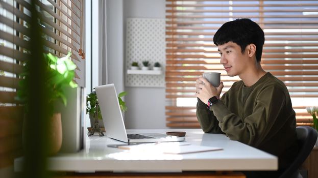 Focused asian businessman watching online webinar on laptop during remote working from home.