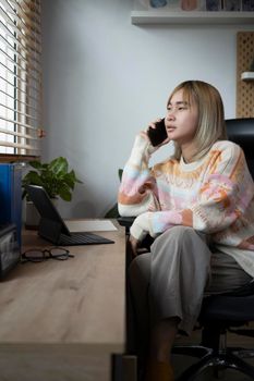 Young woman sitting on comfortable chair at home office and talking on mobile phone.