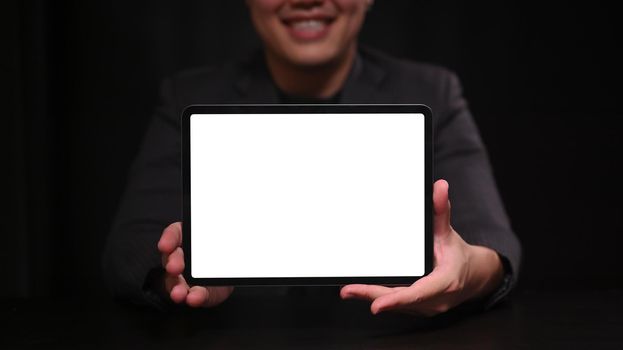 Smiling businessman in suit showing digital table with blank screen.