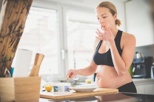 Beautiful sporty fit young pregnant woman preparing healthy meal in home kitchen. Healty lifestyle concept
