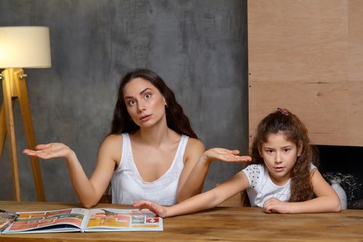 Portrait of a mother helping her small sweet and cute daughter to make her homework indoors. They both are disappointed. Mom is gesticulating and looking up.