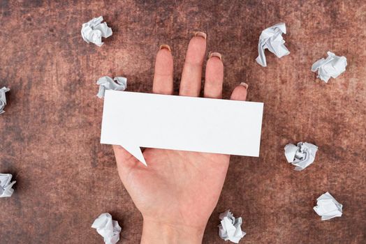 Hand Of Woman Holding Speech Bubble Sheet Surrounded With Crumpled Papers.