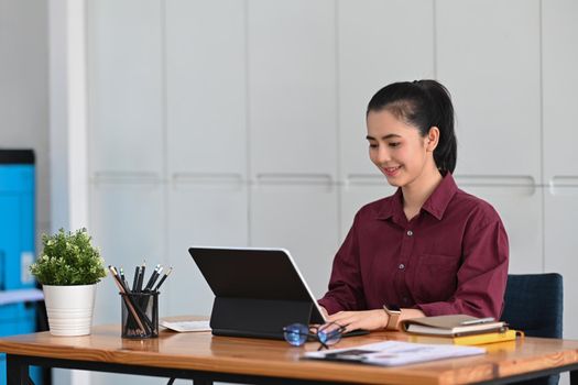 Charming businesswoman sitting in office and searching information on computer tablet.