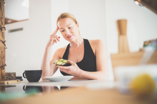 Beautiful sporty fit young pregnant woman having a healthy snack in home kitchen. Healty lifestyle concept