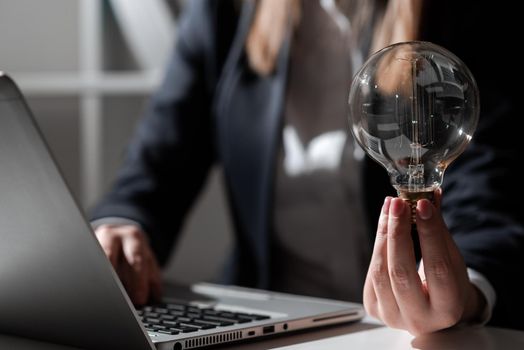 Businesswoman Typing Recent Updates On Lap Top On Desk Holding Lightbulb.