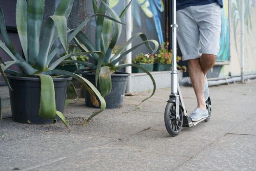 Close up man ride scooter with big wheels having a ride on the streets or park after work outdoors with agave plants on background. No face visible. Focus on front wheel with handle.