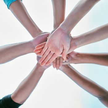 Closeup of diverse group of people from below stacking hands together in a pile to express unity, support and trust. Multiracial community huddled in a circle to celebrate winning achievement. Joining for collaboration and team spirit.