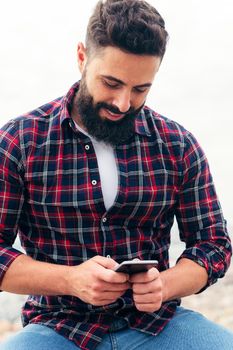 vertical portrait of a handsome bearded man typing a text message on his mobile phone, concept of freedom and technology, copy space for text