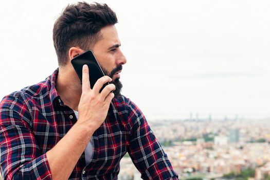portrait of a handsome bearded man talking by mobile phone outdoors, concept of freedom and technology, copy space for text