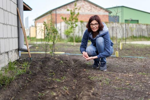 Caucasian adult woman in a home vegetable garden planting seeds