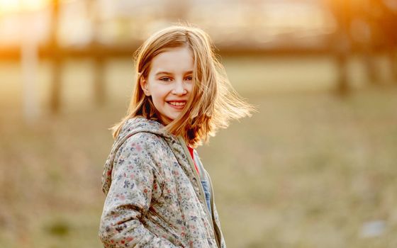 Preteen girl child looking at camera and smiling in amazing sunset light in the field. Beautiful portrait of pretty female kid