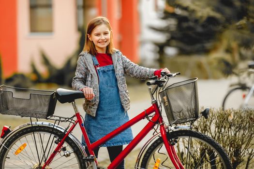 Preteen girl child with bycicle looking at camera and smiling in beautiful sunset light. Pretty kid walking outdoors with vehicle