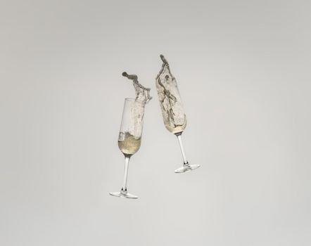 Splash of two crystal glasses toasting with champagne for a celebration. Splash on white cut-out background. graphic resource.