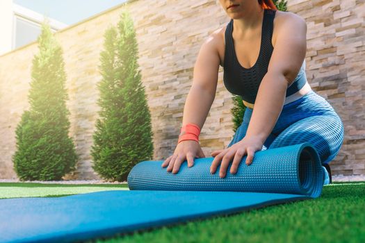 cropped shot of a young sportswoman, unrolling a mat for yoga exercises. unrecognisable girl doing sports exercises at home. concept of health and wellness. natural light in the garden.