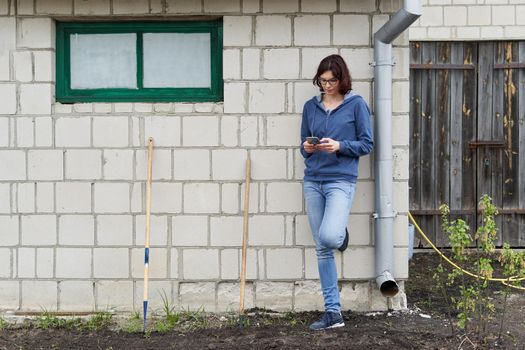 Caucasian woman standing next to a home vegetable garden using the mobile