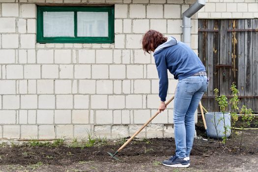 Back of a caucasian woman digging the soil with a hoe in a vegetable garden