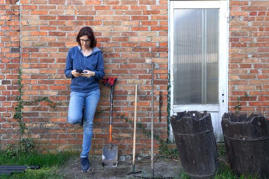 Woman using a mobile while leaning next to tools for work the land