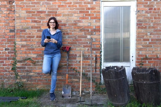 Woman looking at camera while using a mobile next to tools for work the land