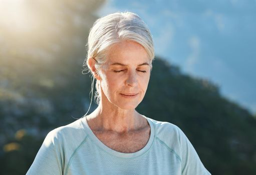 Senior woman with grey hair standing outside with her eyes closed and breathing deeply, meditating in nature. Finding inner peace, balance and living healthy.