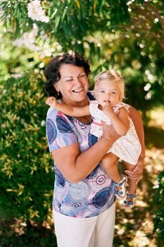 Laughing aged woman holds a little girl in her arms. High quality photo