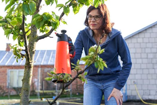 Woman standing with serious expression while fumigating plants in a home garden