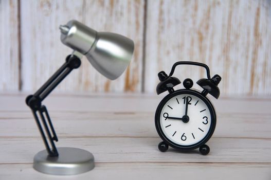Alarm clock pointing at 9 o'clock with table lamp on wooden background. Copy space and time concept