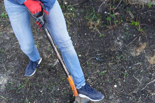 Top view photo of the legs and shoe of a person pressing a hoe to plough the land