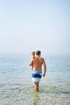 Dad with a little girl in his arms walks through the shallow sea. High quality photo