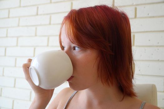 red-haired teenage girl drinks tea from a white cup close-up