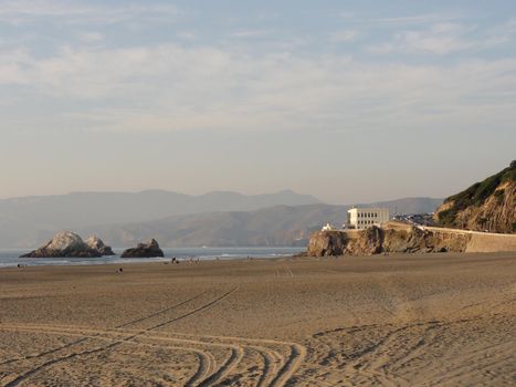 Ocean Beach, looking towrd the cliff house, in San Francisco on a clear day.  Sparsely populated, with tire tracks visble in the sand.