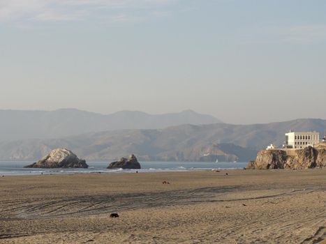 Ocean Beach, looking towrd the cliff house, in San Francisco on a clear day.  Sparsely populated, with tire tracks visble in the sand.