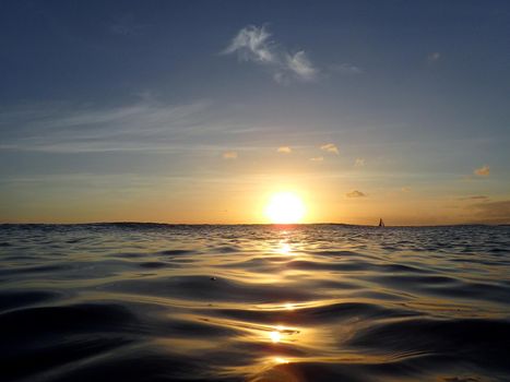 Dramatic lighting the sky and ocean during sunsets with light reflecting on ocean waves moving with boats on the water in the distance off Waikiki with clouds on Oahu, Hawaii.