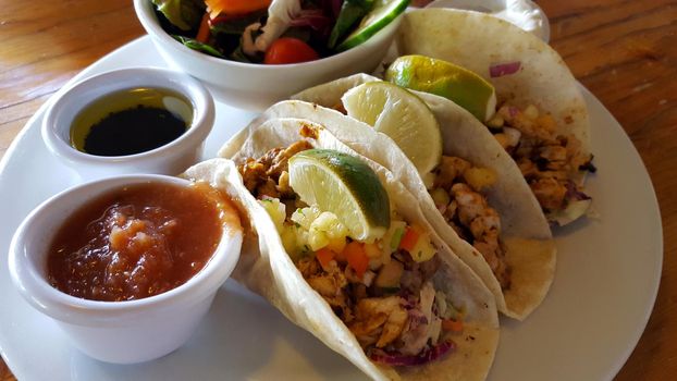 ISLAND FISH TACOS: blackened island fish, flour tortilla, mixed cabbage, black bean, chipotle aioli, tropical fruit salsa, red salsa, sour cream and side salad on wood table