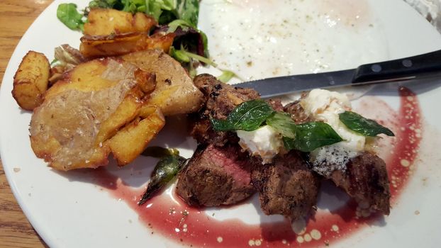 Kalbi Steak, eggs, and fried potatoes on a late with a knife.