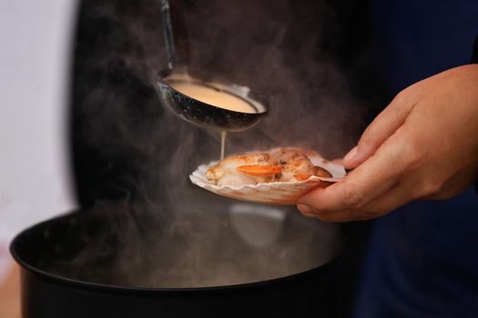 The seller pours white sauce on the scallops