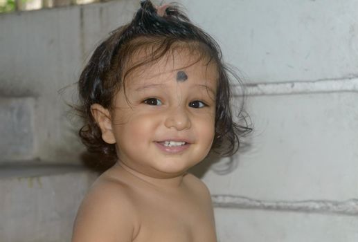 Cute happy indian baby without shirt smiling and looking at camera.