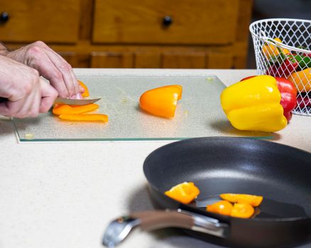 Cook slices orange bell pepper on cutting board.