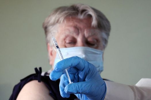 An elderly woman at the doctor's appointment is vaccinated. Syringe with vaccine close-up. The concept of vaccination against Covid19..