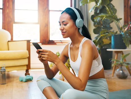 a sporty young woman wearing headphones and using a cellphone while exercising at home.