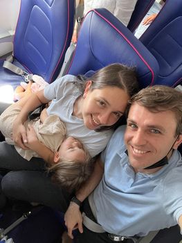 Dad and mom with a sleeping daughter in her arms sit in airplane seats. High quality photo