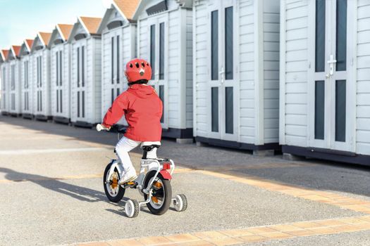 Girl in a helmet learns riding a four-wheeled bicycle near the changing cabins