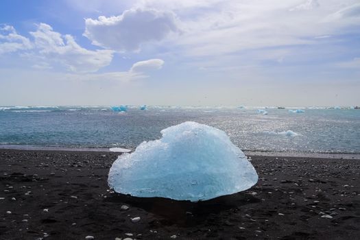 Diamond Beach in Iceland with blue icebergs melting on black sand and ice glistening with sunlight