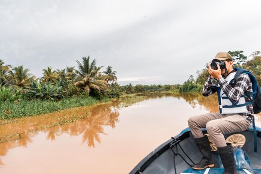 Latino man sailing a boat down a muddy river and taking pictures in El Rama, Nicaragua